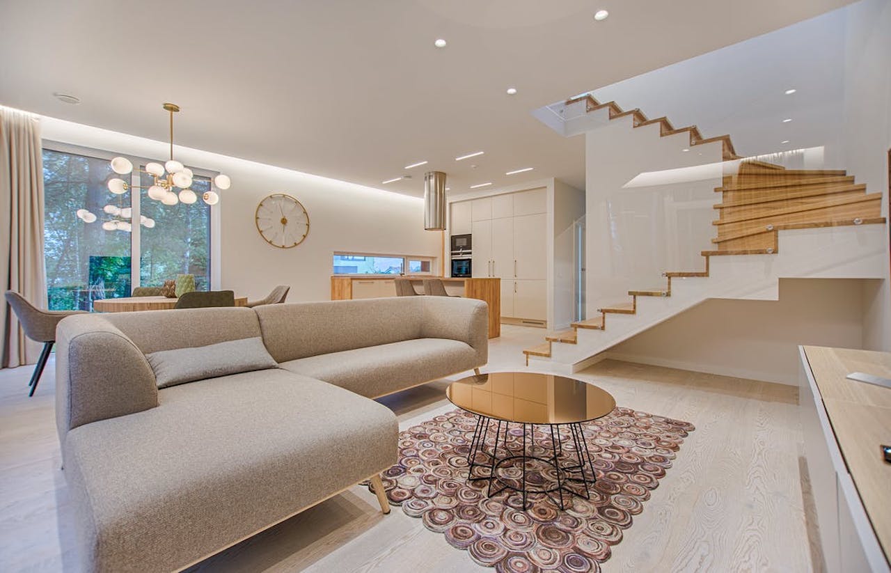 Photo of a white living room with an L shaped couch and an elegant staircase to the right of the couch. 